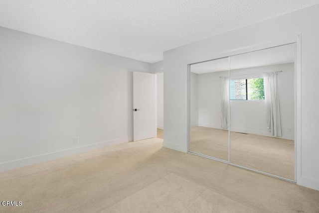 unfurnished bedroom featuring light carpet, a textured ceiling, and a closet