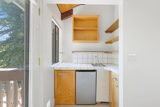 kitchen with plenty of natural light, sink, tile counters, and stainless steel fridge