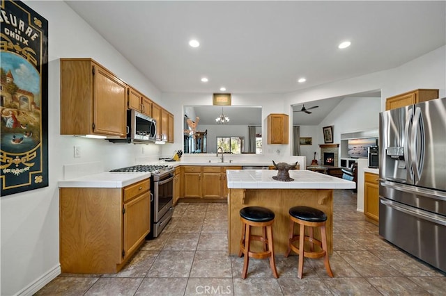 kitchen featuring a center island, tile counters, appliances with stainless steel finishes, a sink, and a warm lit fireplace