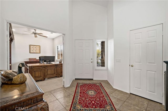 foyer entrance with a towering ceiling, baseboards, a ceiling fan, and light tile patterned flooring