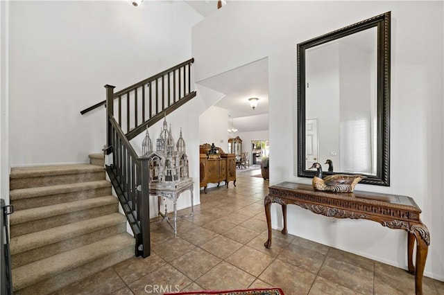 foyer entrance featuring baseboards, a towering ceiling, stairway, tile patterned floors, and a notable chandelier