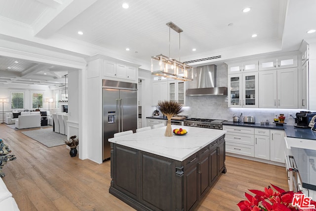 kitchen featuring wall chimney range hood, range, built in refrigerator, hanging light fixtures, and dark brown cabinetry