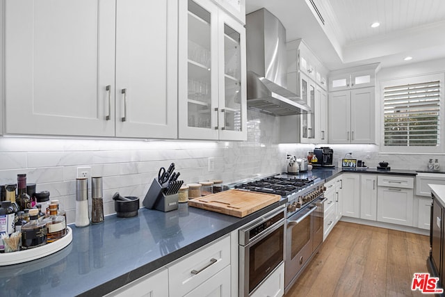 kitchen featuring crown molding, white cabinetry, double oven range, a raised ceiling, and wall chimney exhaust hood