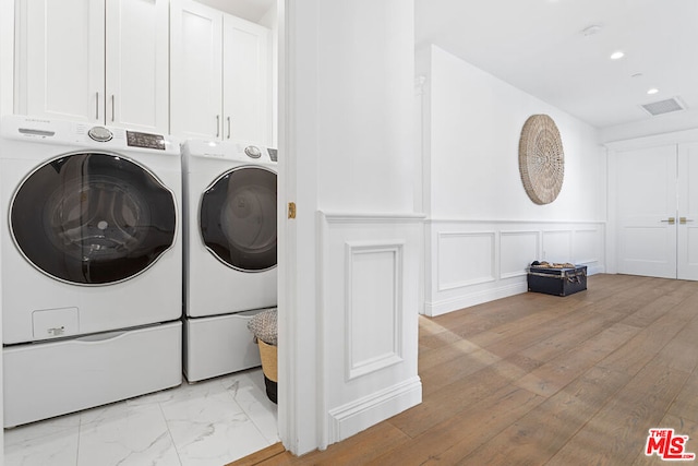 clothes washing area featuring cabinets, washer and dryer, and light hardwood / wood-style flooring