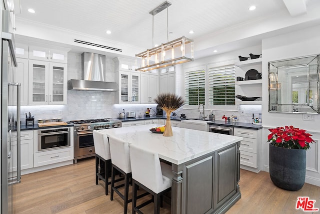 kitchen with high end range, wall chimney range hood, white cabinets, and a kitchen island