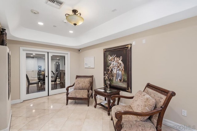 living area with french doors, a raised ceiling, and light tile patterned flooring