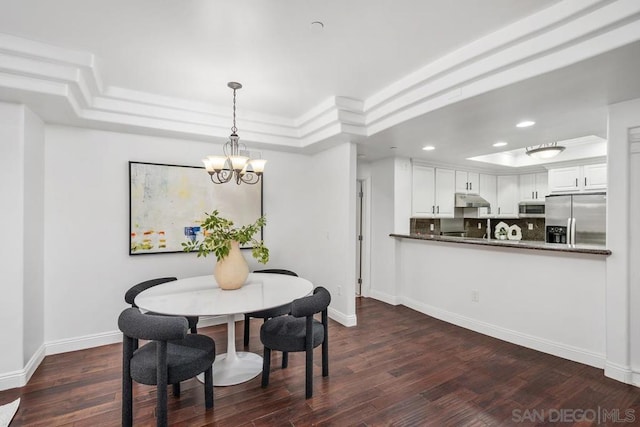 dining room featuring dark hardwood / wood-style floors, a raised ceiling, and a notable chandelier