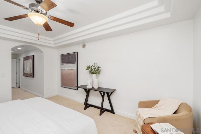 carpeted bedroom with a raised ceiling and ceiling fan