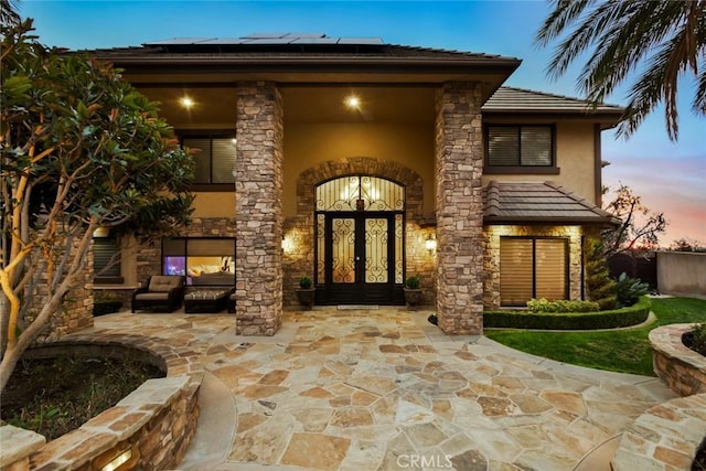 exterior entry at dusk with french doors, outdoor lounge area, and a patio