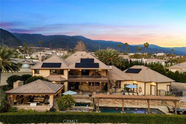 back house at dusk featuring a gazebo, a patio area, solar panels, a mountain view, and a balcony