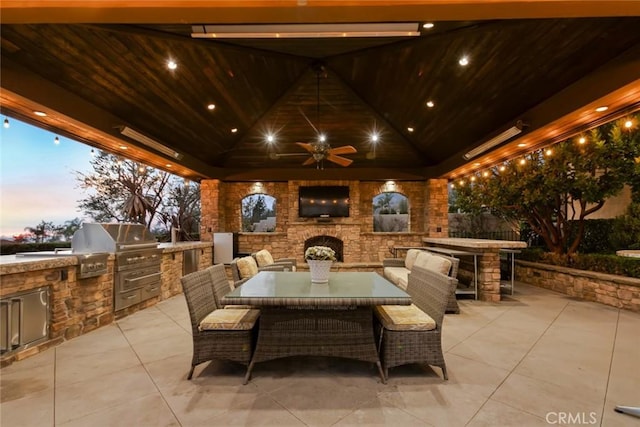 patio terrace at dusk featuring an outdoor stone fireplace, ceiling fan, a gazebo, a grill, and area for grilling