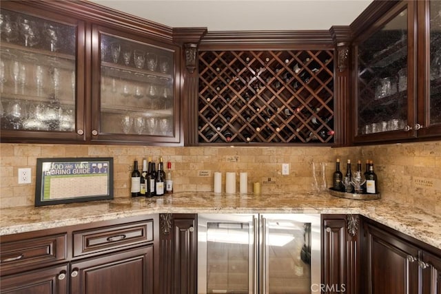 bar with beverage cooler, light stone countertops, and dark brown cabinets