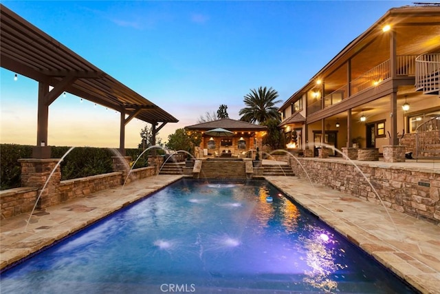 pool at dusk featuring pool water feature, a patio, a bar, and a gazebo