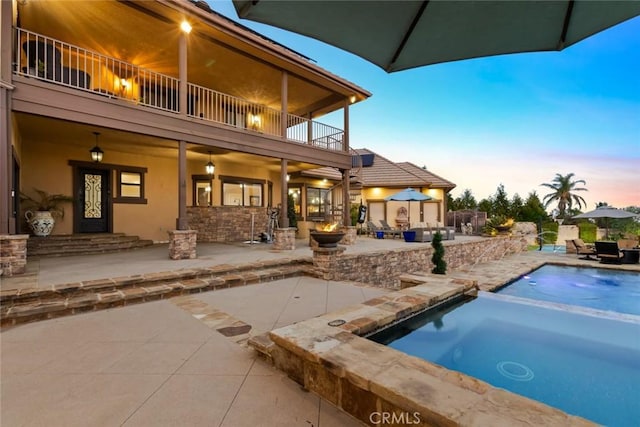 pool at dusk with a patio and an in ground hot tub