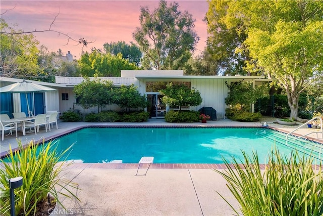 pool at dusk with a patio area and a diving board