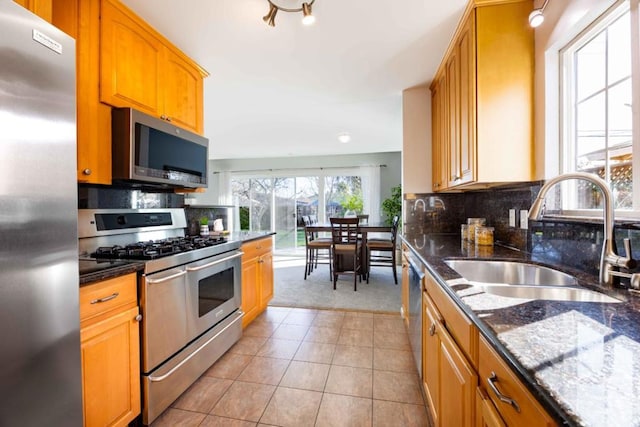 kitchen featuring sink, light tile patterned floors, dark stone countertops, stainless steel appliances, and backsplash