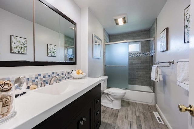 full bathroom with combined bath / shower with glass door, tasteful backsplash, wood-type flooring, vanity, and toilet