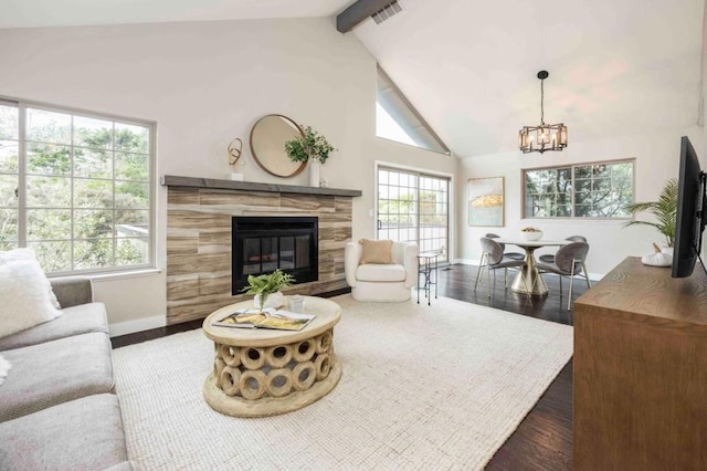 living room featuring dark wood-type flooring, high vaulted ceiling, a notable chandelier, a tiled fireplace, and beamed ceiling