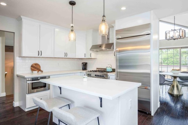 kitchen with stainless steel appliances, dark wood-type flooring, white cabinets, and decorative light fixtures