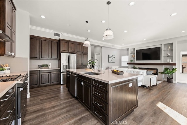 kitchen featuring decorative light fixtures, sink, dark brown cabinetry, stainless steel appliances, and a center island with sink