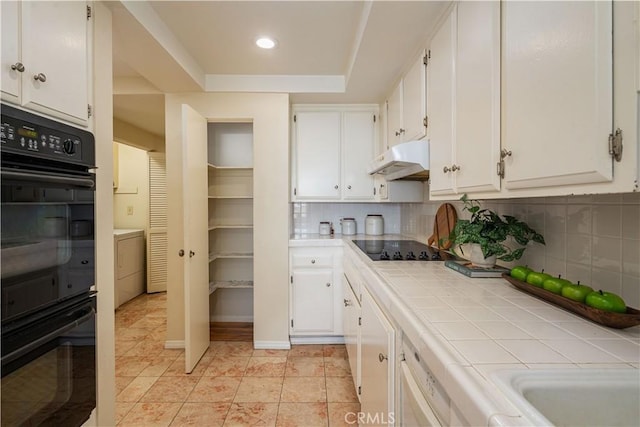 kitchen featuring backsplash, a tray ceiling, tile counters, black appliances, and white cabinets