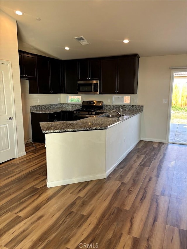 kitchen with sink, gas range, wood-type flooring, dark stone countertops, and kitchen peninsula