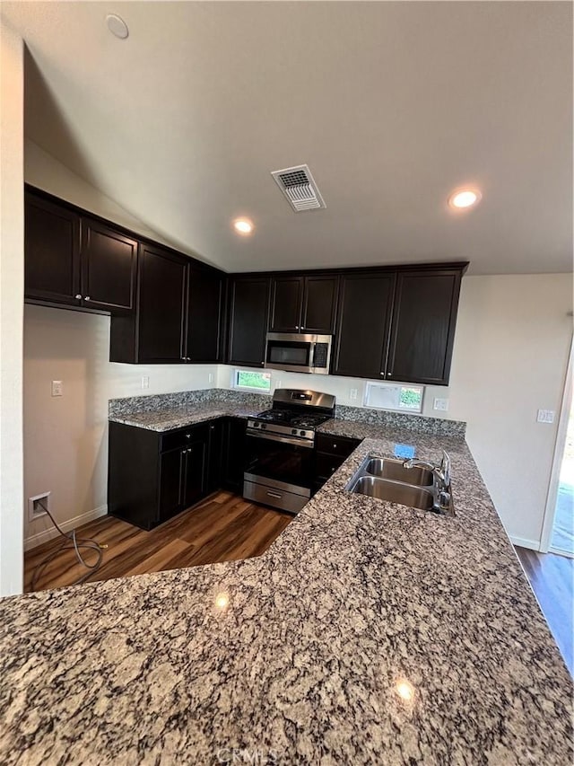 kitchen with dark wood-type flooring, sink, light stone counters, appliances with stainless steel finishes, and kitchen peninsula