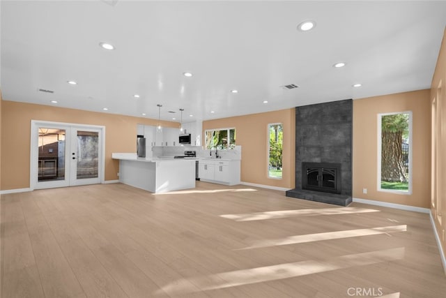 unfurnished living room with french doors, sink, a tile fireplace, and light hardwood / wood-style flooring