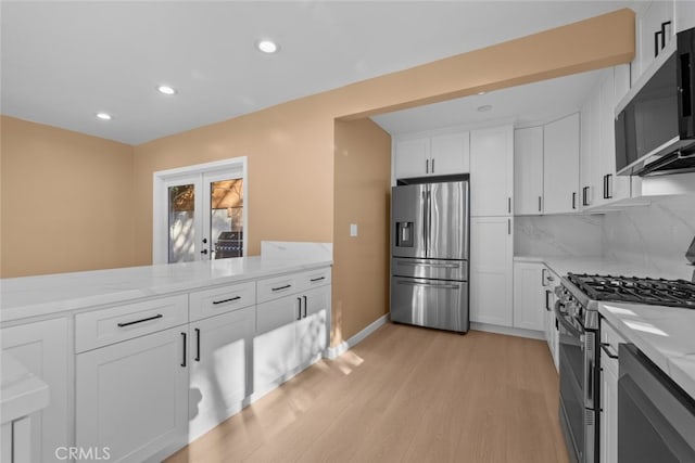 kitchen with tasteful backsplash, white cabinets, light stone counters, stainless steel appliances, and light hardwood / wood-style flooring