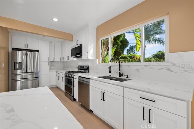 kitchen with appliances with stainless steel finishes, light stone countertops, sink, and white cabinets