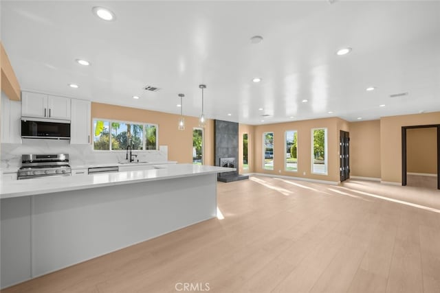 kitchen with sink, white cabinets, hanging light fixtures, light hardwood / wood-style floors, and stainless steel appliances