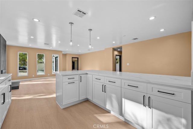 kitchen with white cabinetry, hanging light fixtures, light stone counters, and light hardwood / wood-style floors