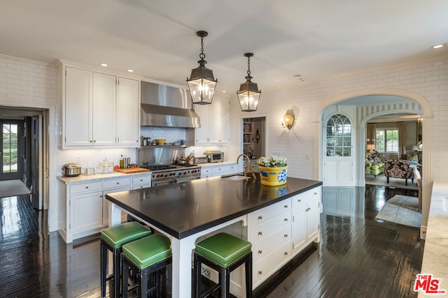 kitchen featuring sink, white cabinets, a center island with sink, exhaust hood, and range with two ovens