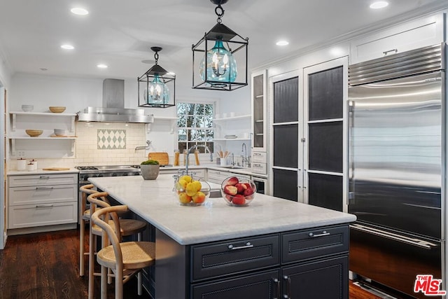 kitchen featuring an island with sink, white cabinetry, a kitchen breakfast bar, stainless steel appliances, and wall chimney range hood