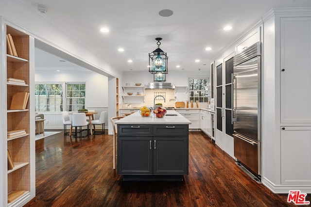 kitchen with hanging light fixtures, built in fridge, a wealth of natural light, a kitchen island with sink, and white cabinets