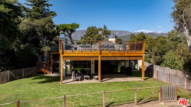 rear view of house featuring a deck with mountain view, a patio area, and a lawn