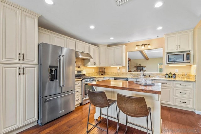 kitchen featuring appliances with stainless steel finishes, butcher block countertops, sink, a kitchen breakfast bar, and dark wood-type flooring