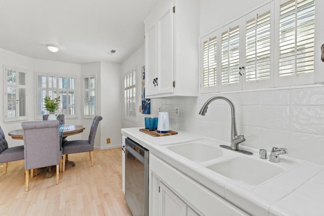 kitchen featuring tile countertops, dishwasher, sink, white cabinets, and backsplash