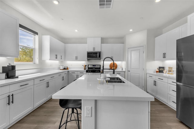 kitchen featuring wood-type flooring, appliances with stainless steel finishes, a center island with sink, and white cabinets