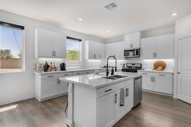 kitchen with sink, white cabinets, stainless steel appliances, a center island with sink, and light wood-type flooring