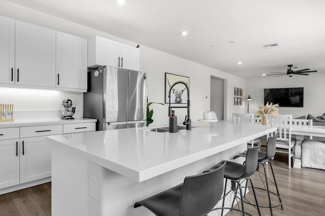 kitchen with sink, stainless steel refrigerator, a breakfast bar, white cabinetry, and a spacious island