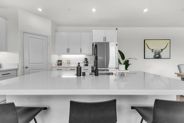 kitchen with a kitchen breakfast bar, white cabinetry, sink, and stainless steel refrigerator