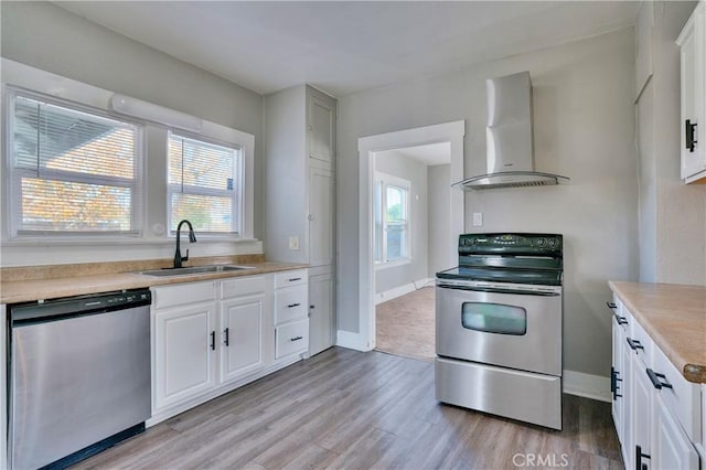 kitchen with appliances with stainless steel finishes, white cabinetry, sink, wall chimney range hood, and light wood-type flooring