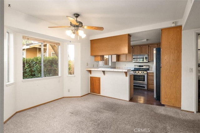 kitchen with a kitchen bar, dark colored carpet, tile countertops, kitchen peninsula, and stainless steel appliances