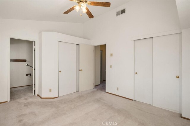 unfurnished bedroom with vaulted ceiling, light carpet, and two closets