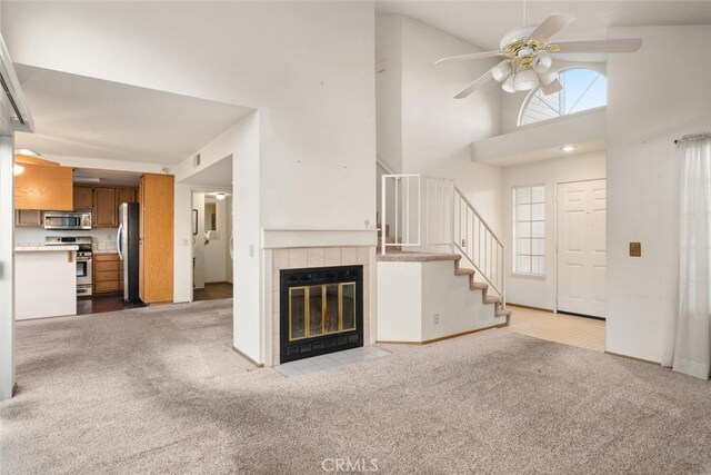 unfurnished living room featuring a tiled fireplace, high vaulted ceiling, light colored carpet, and ceiling fan