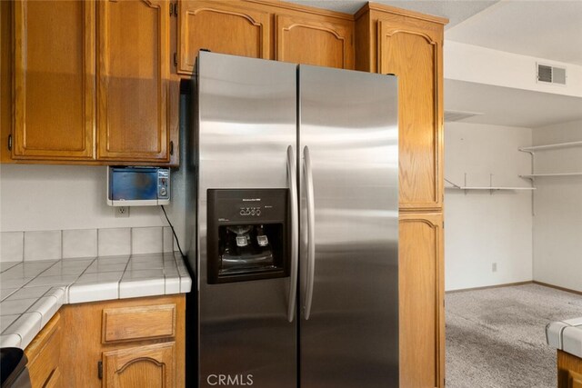 kitchen with stainless steel refrigerator with ice dispenser, tile counters, and light colored carpet