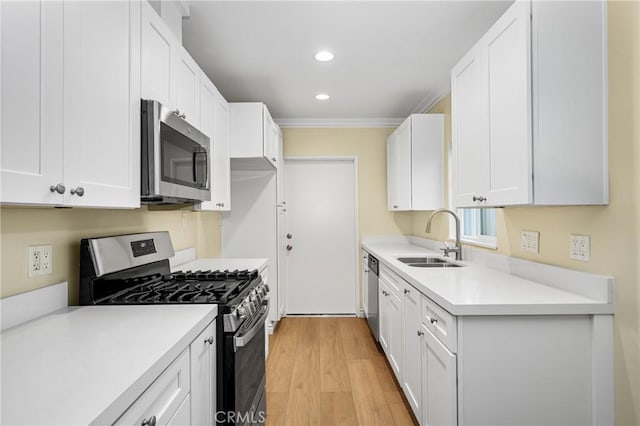 kitchen with sink, stainless steel appliances, ornamental molding, white cabinets, and light wood-type flooring