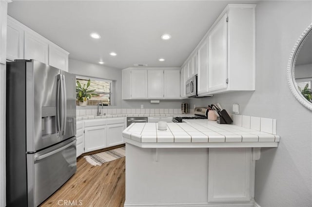 kitchen with a breakfast bar area, tile counters, kitchen peninsula, stainless steel appliances, and white cabinets