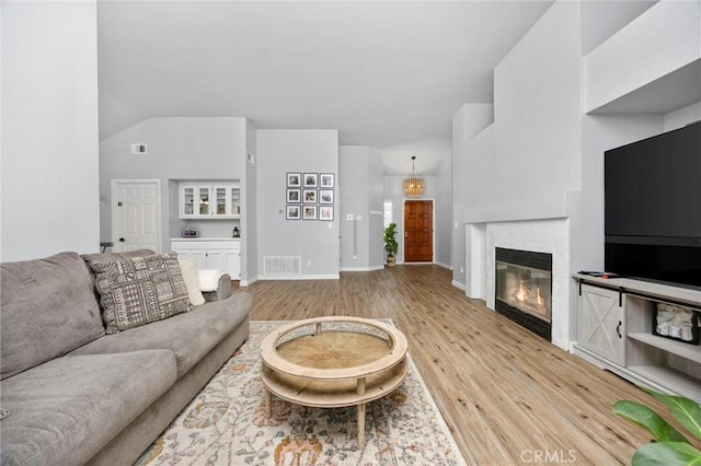 living room with a tiled fireplace, vaulted ceiling, and light hardwood / wood-style floors